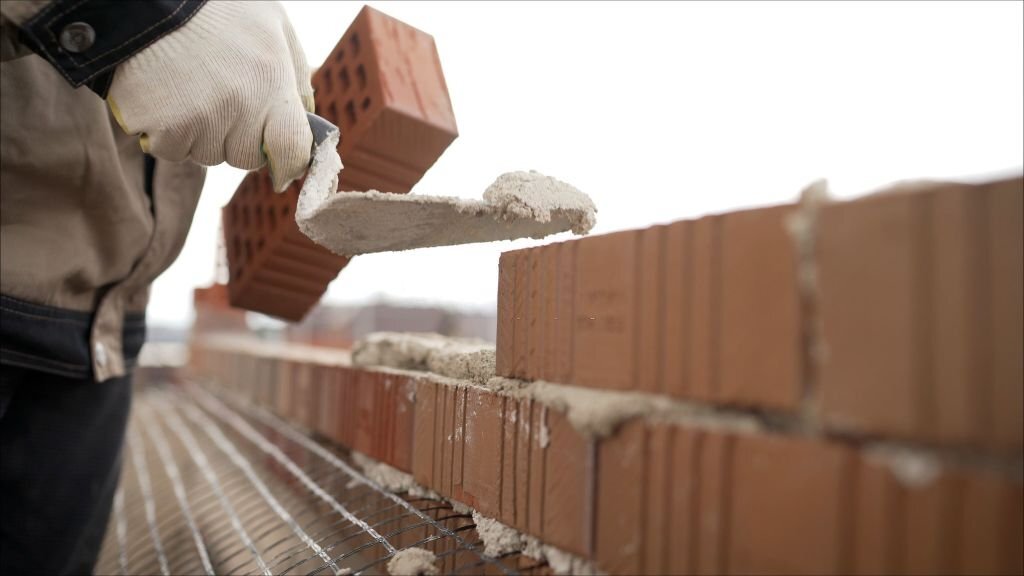 Bricklayer working in construction site of a brick wall. Bricklayer putting down another row of bricks in site. Worker puts a brick wall