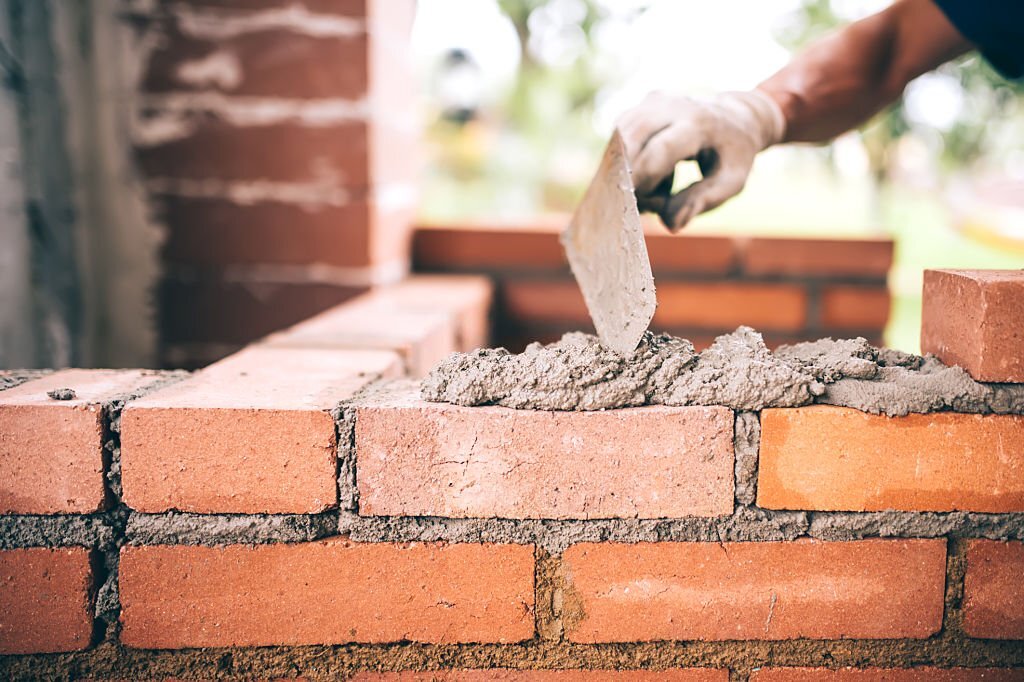 industrial Construction bricklayer worker building walls with bricks, mortar and putty knife